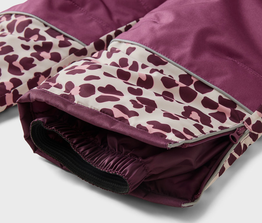 Gros plan sur le bas d'un pantalon de ski prune et imprimé léopard, montrant une fermeture éclair, une bande réfléchissante et un revers intérieur élastique.