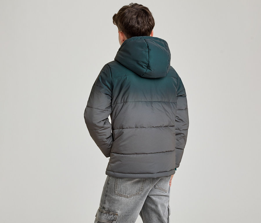 Un jeune homme vu de dos, portant une doudoune à capuche avec un dégradé du sarcelle foncé au gris foncé, et un jean gris. Ses mains sont dans ses poches.