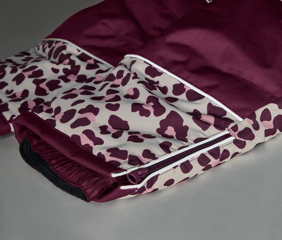 Gros plan sur un vêtement en tissu bordeaux et imprimé léopard. L'imprimé léopard, beige avec des taches rose foncé, est séparé du bordeaux uni par une bande blanche. Une fermeture éclair bordeaux et une manchette élastique sont visibles sur la partie imprimée léopard.