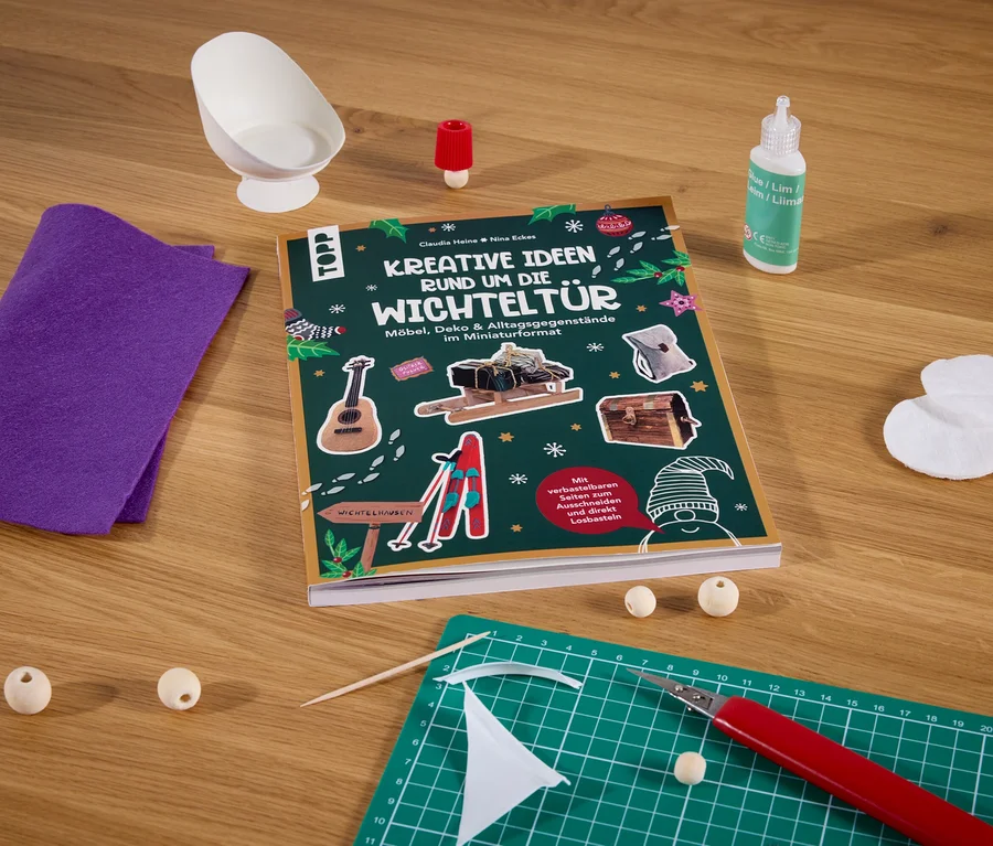 Le livre »Kreative Ideen rund um die Wichteltür« est posé sur une table avec d'autres fournitures de bricolage.