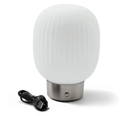 Une lampe de table à LED avec accumulateur et abat-jour en verre est posée à côté d'un câble de chargement noir.