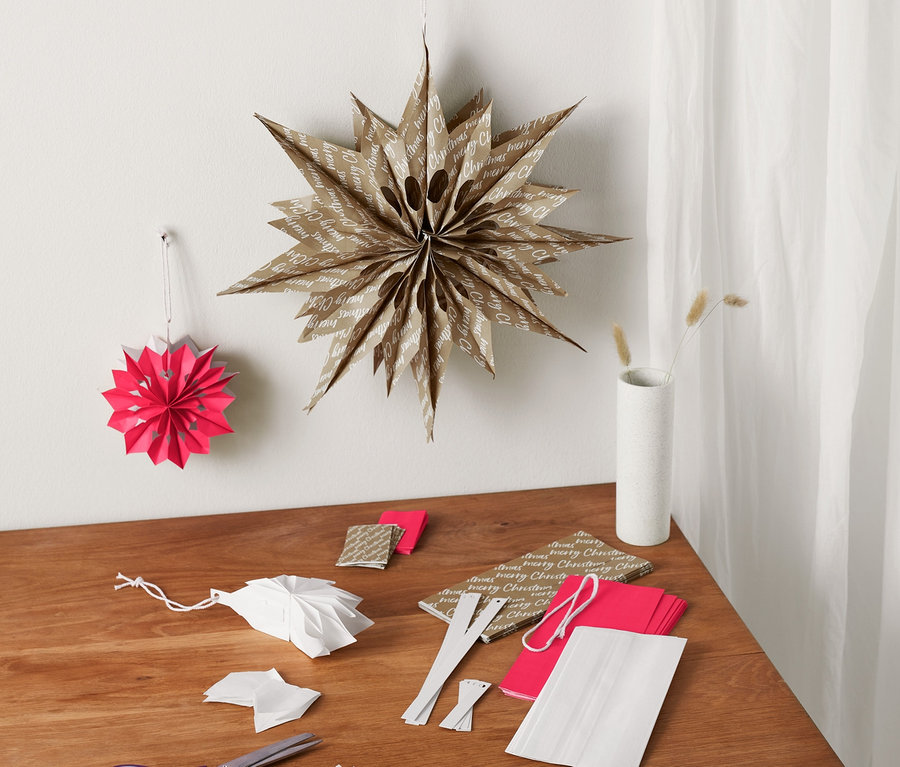 Sur une table se trouvent un kit pour bricoler des étoiles en sachet en papier et des décorations finies.