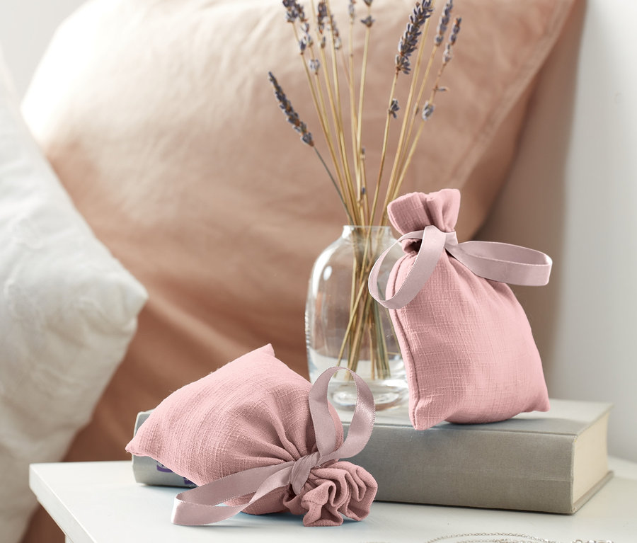 Deux sachets parfumés posés sur un livre à côté d'un vase avec de la lavande.
