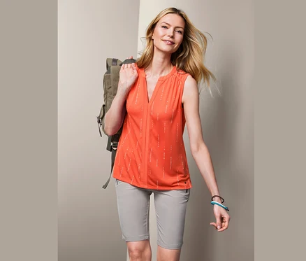 Une femme blonde avec un sac à dos sur l'épaule porte un top fonctionnel orange.