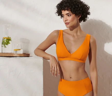 Femme posant en haut de bikini orange à surface structurée.