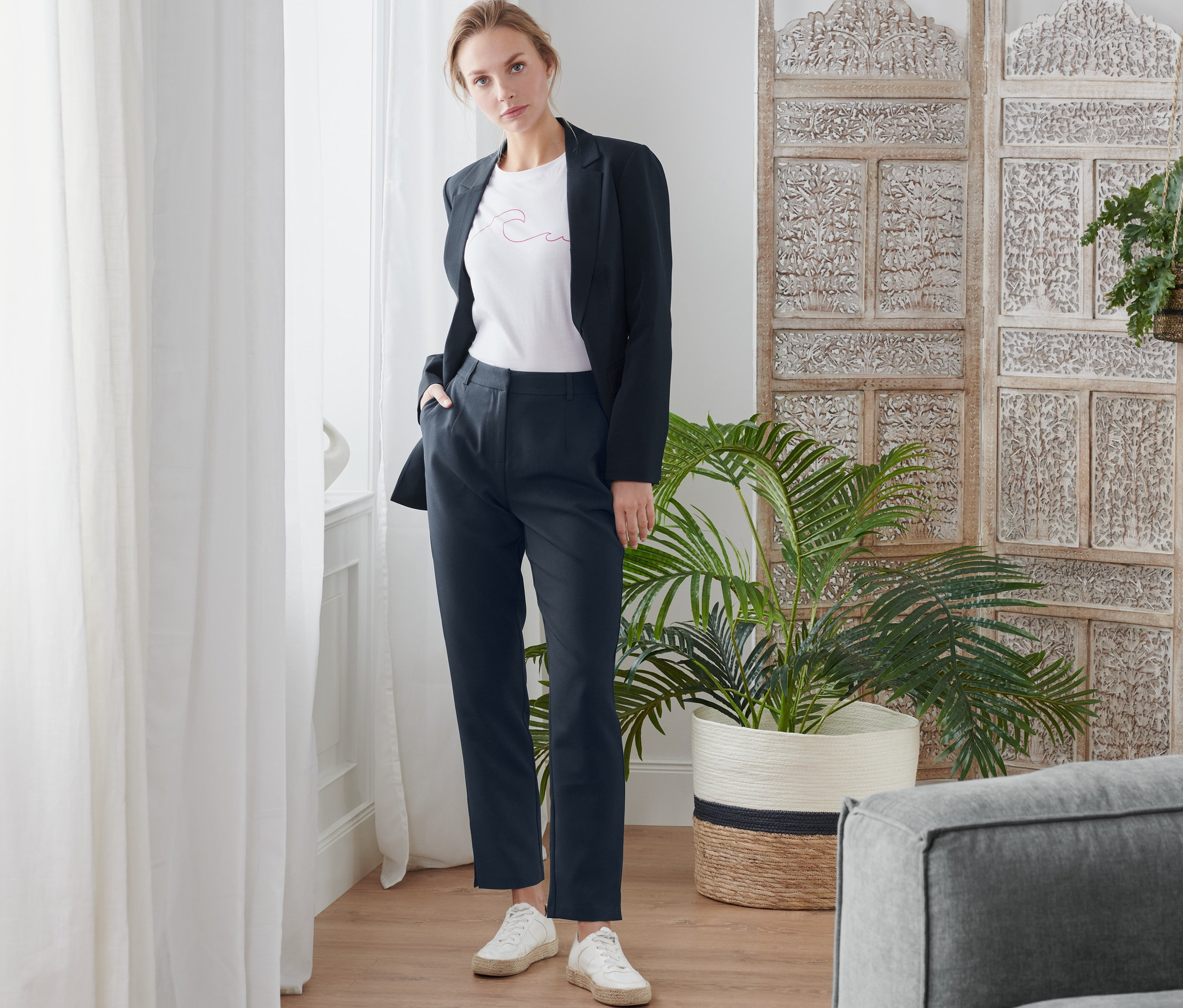 Femme posant en blazer foncé et pantalon tissé.