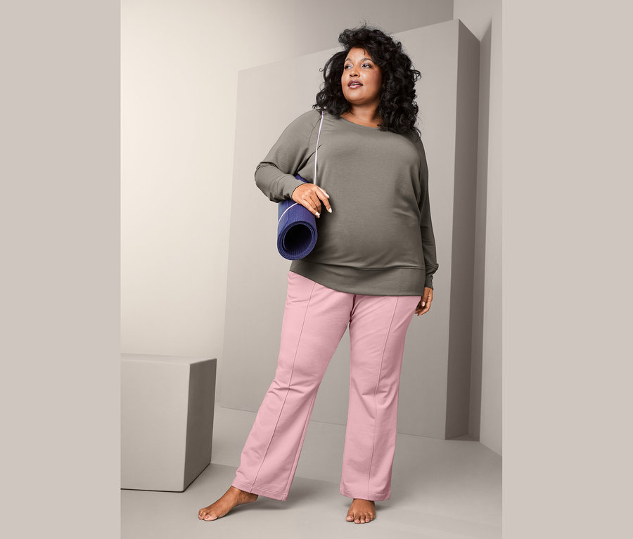 Femme portant un sweat-shirt de yoga et un pantalon de survêtement, tenant un tapis de yoga.