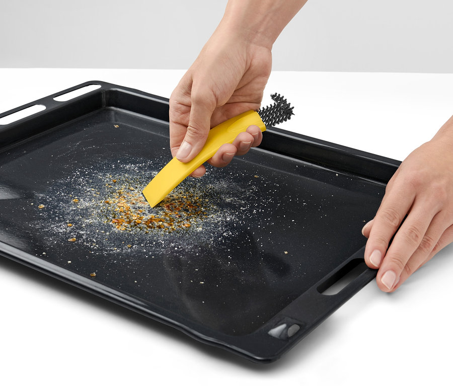 Des mains nettoient une plaque de cuisson avec une brosse à four avec racloir.