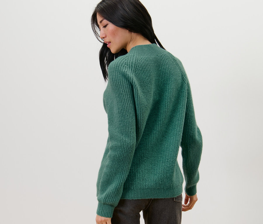 Une femme, vue de dos, porte un pull vert à col droit en grosse maille.
