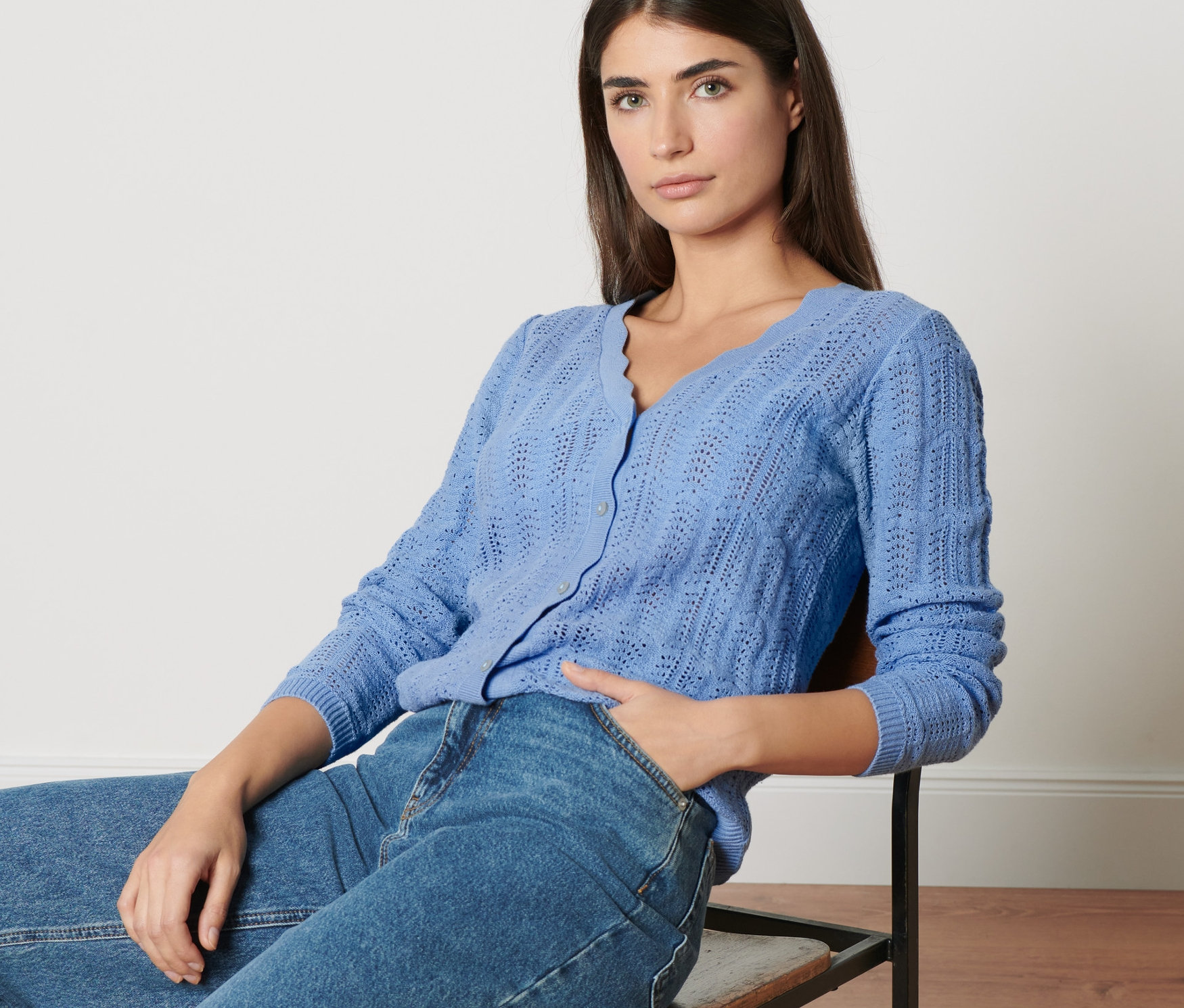 Une femme est assise sur une chaise et porte une veste en maille à motif ajouré et un jean.