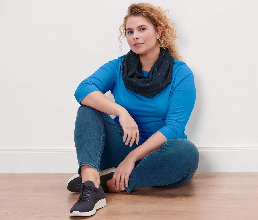 Une femme est assise par terre et porte un t-shirt manches 3/4, bleu azur, un tregging «
Fit Nelly
» et une écharpe-tube à pois.