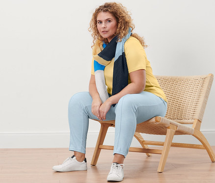 Femme assise sur un fauteuil en osier portant un T-shirt basique jaune et un pantalon de jogging avec nervure.