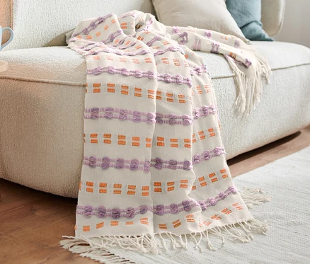 Sur un canapé beige se trouve une couverture avec des détails violets et orange.