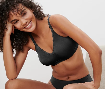 Femme souriante assise sur une chaise portant un soutien-gorge doux Seamless noir.
