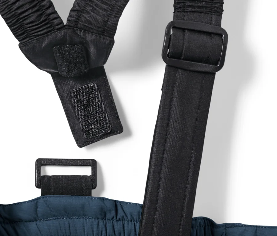 Détail d'un pantalon de ski enfant bleu marine avec bretelles élastiques noires et boucles.