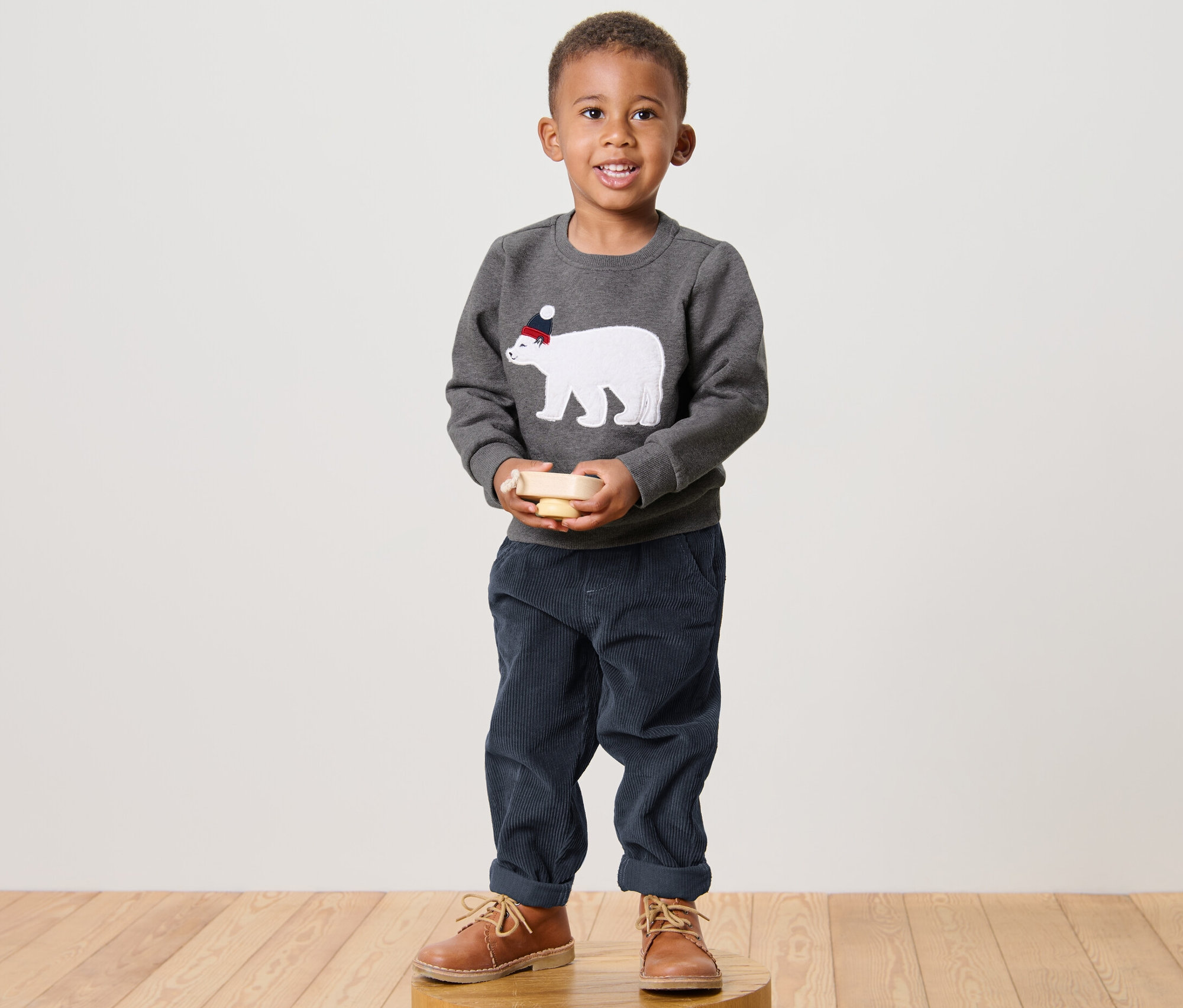Garçon debout tenant un jouet en bois. Il porte un Sweatshirt enfant avec un ours polaire.