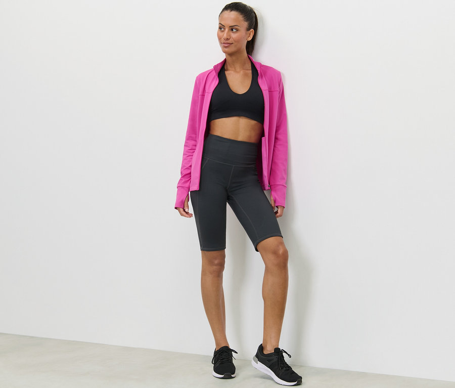 Femme posant en soutien-gorge de sport, cycliste et veste rose.