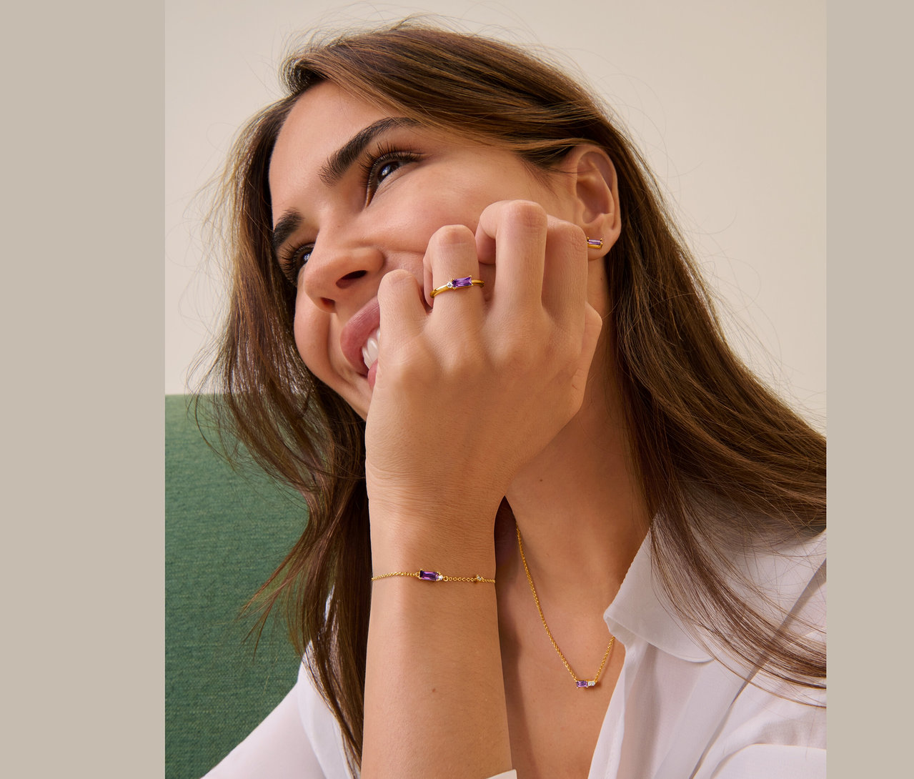 Une femme souriante touche son visage avec sa main, elle porte une bague, des clous d'oreilles, un bracelet et une chaîne en argent 925.