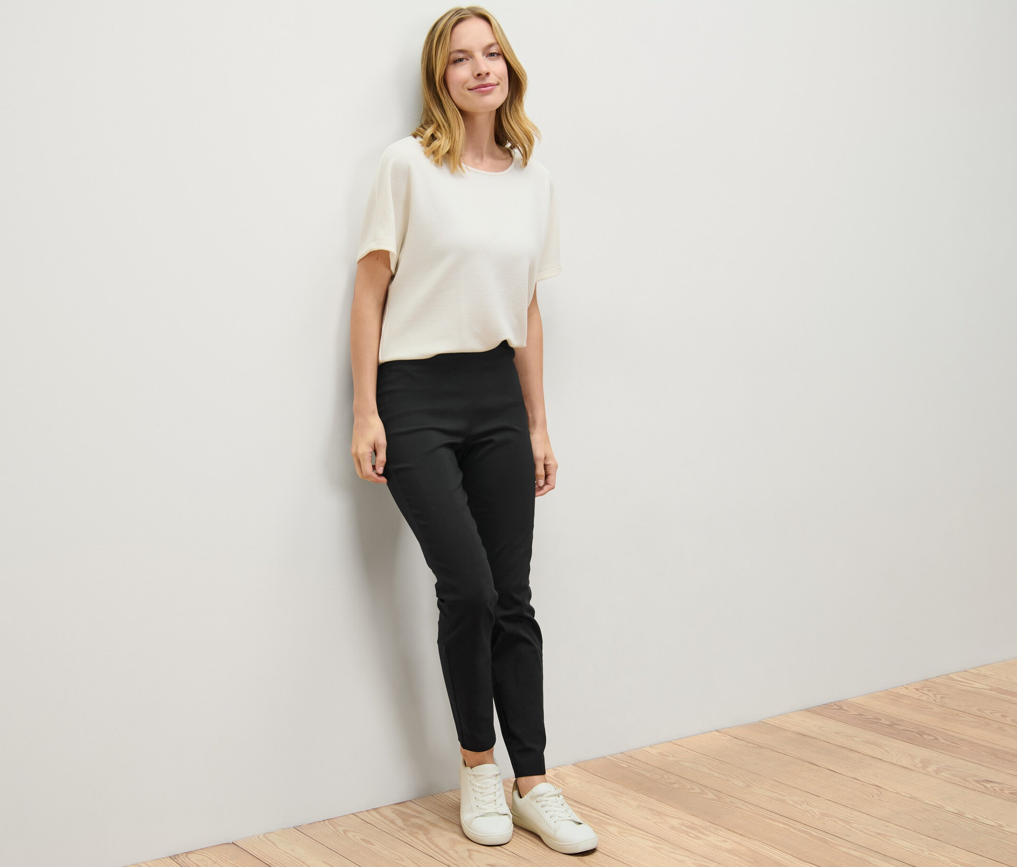 Une femme appuyée contre un mur porte un pantalon stretch noir.