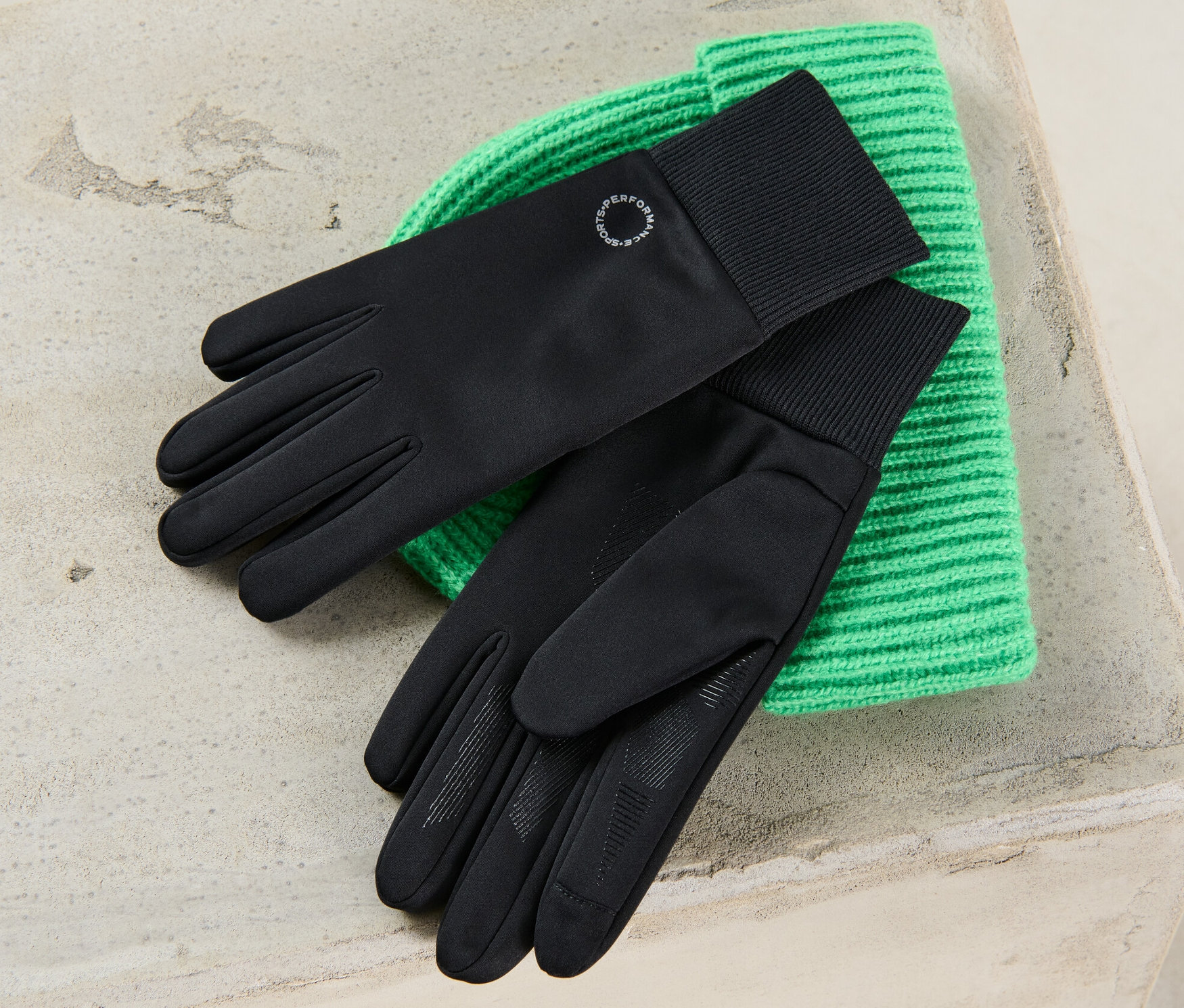 Des gants coupe-vent noirs reposent sur un bonnet en tricot vert.