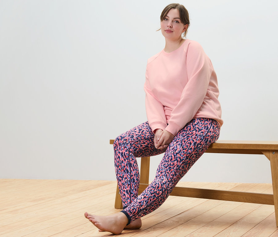 Femme assise sur un banc portant un sweatshirt de yoga rose et un legging de sport réversible rose/bleu marine.