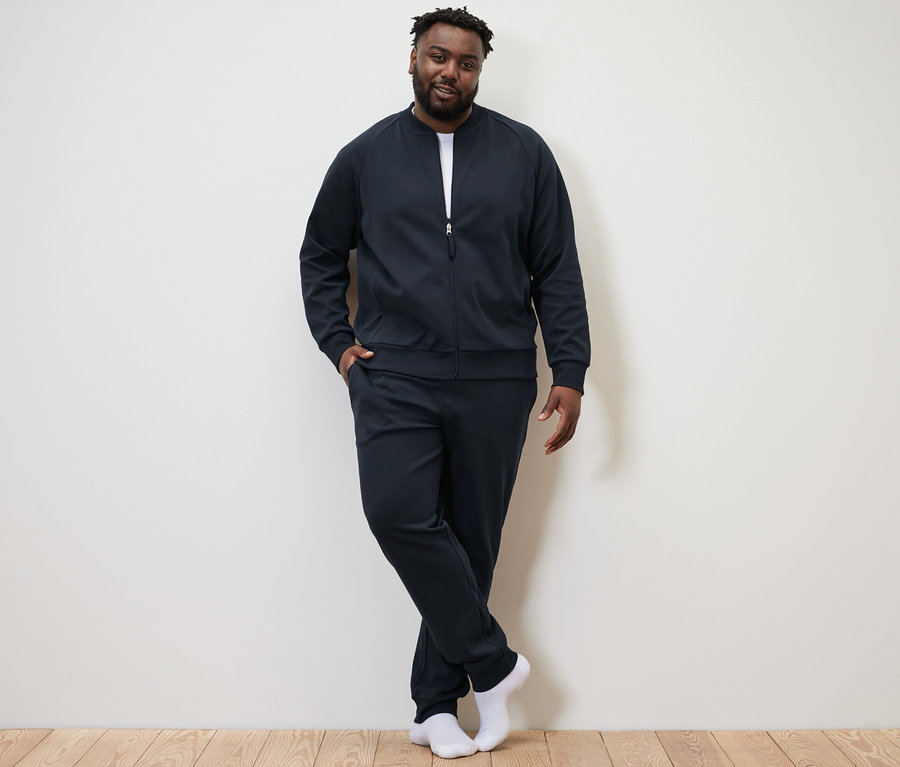 Un homme pose devant un mur et porte un survêtement d’intérieur bleu marine.