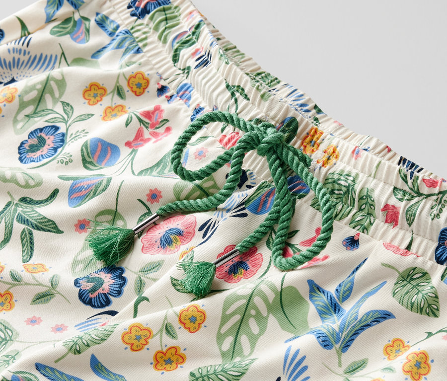 Détail d'un pantalon de pyjama à motif floral avec un cordon de serrage vert à la taille.