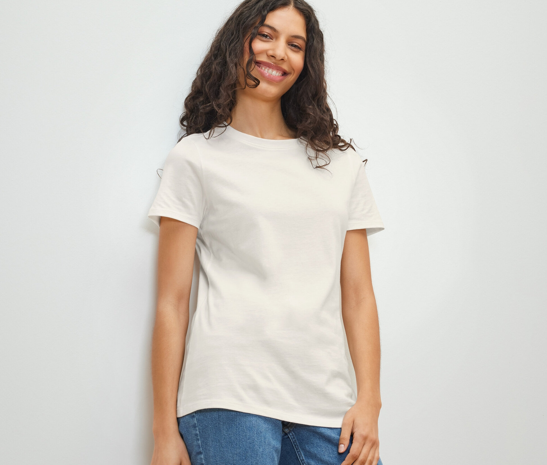 Une femme souriante porte un t-shirt basique blanc et un jean.