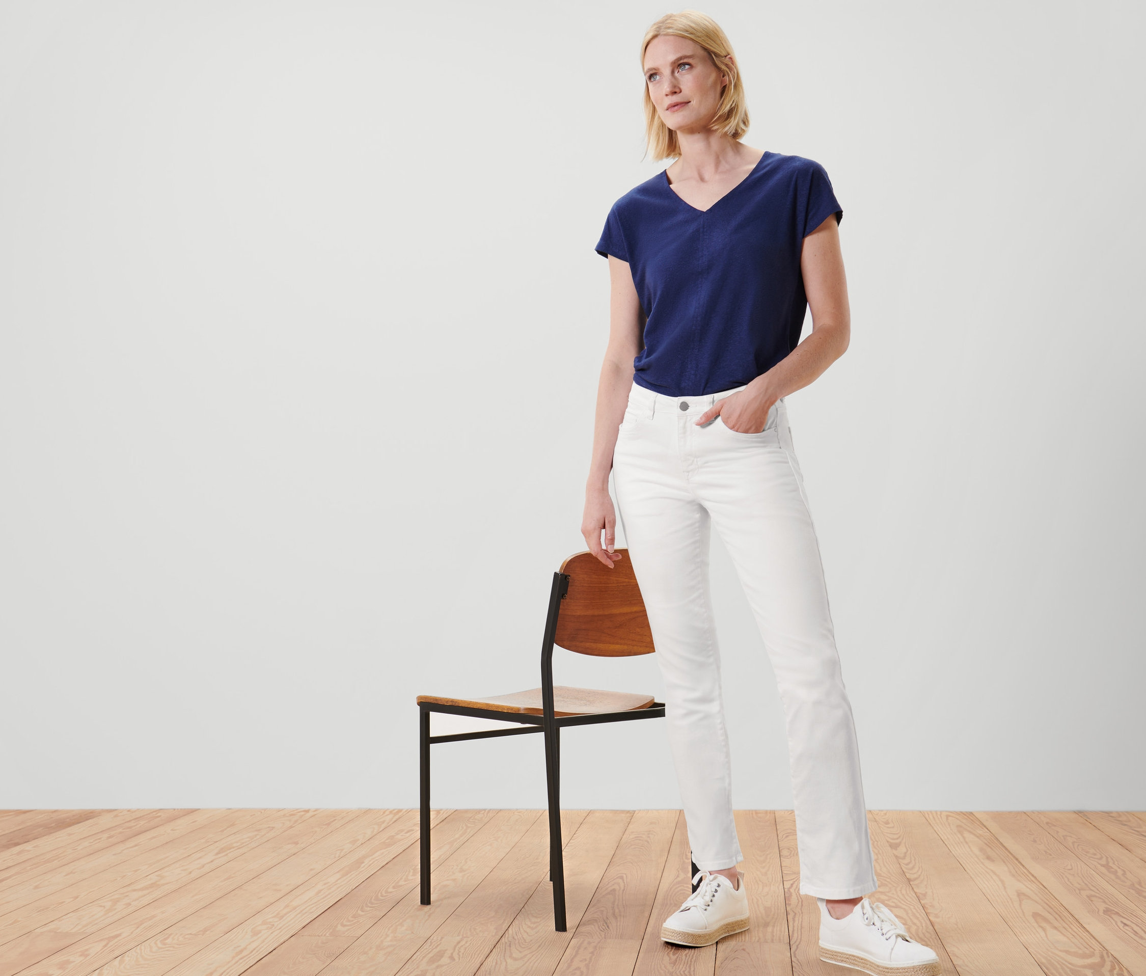 Une femme pose à côté d'une chaise et porte un jean – Fit « Kira » et un pantalon tissé.