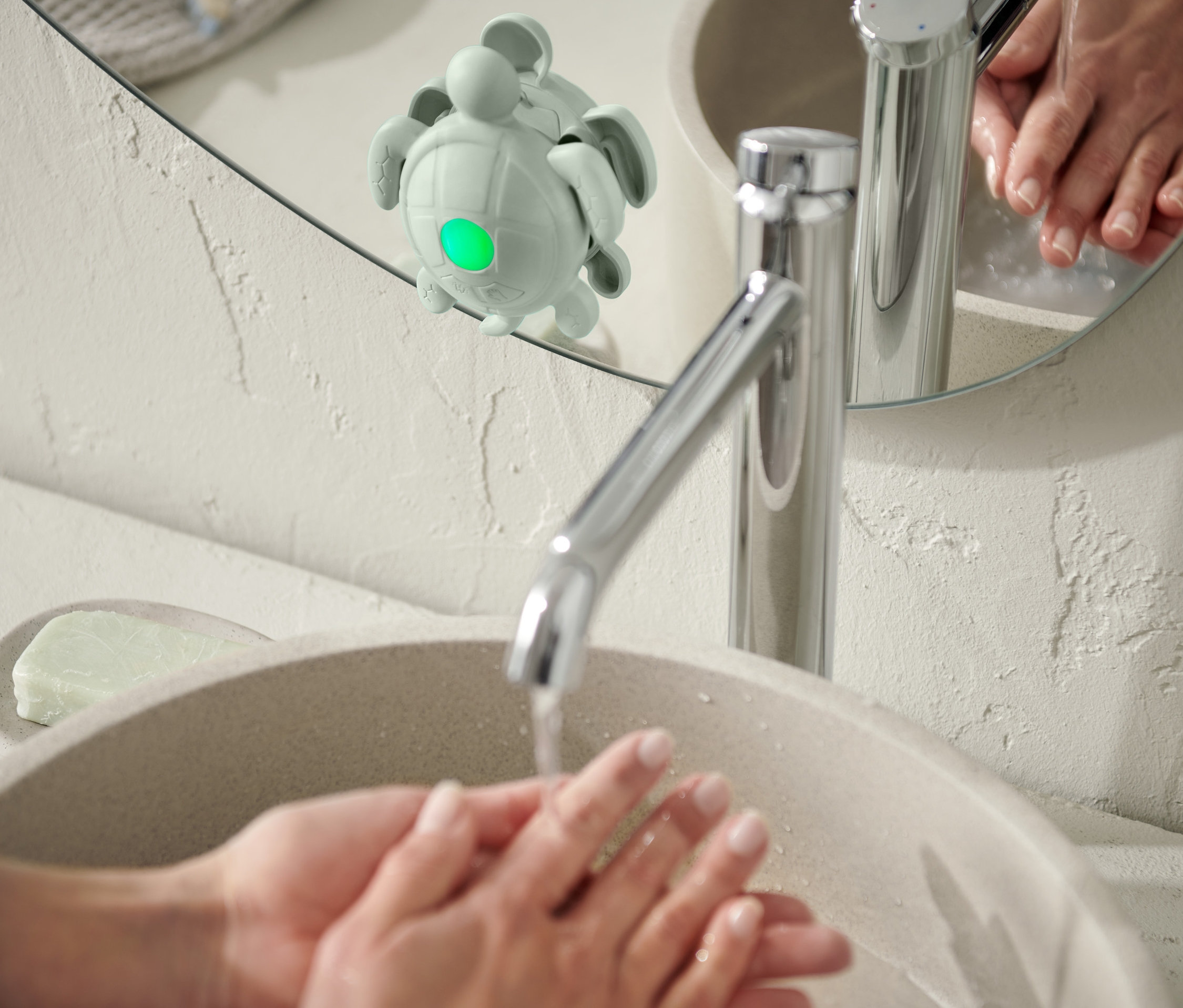 Une personne se lave les mains dans un lavabo ; un minuteur pour se laver les mains et les dents est fixé à un miroir.