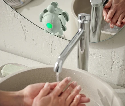 Une personne se lave les mains dans un lavabo ; un minuteur pour se laver les mains et les dents est fixé à un miroir.