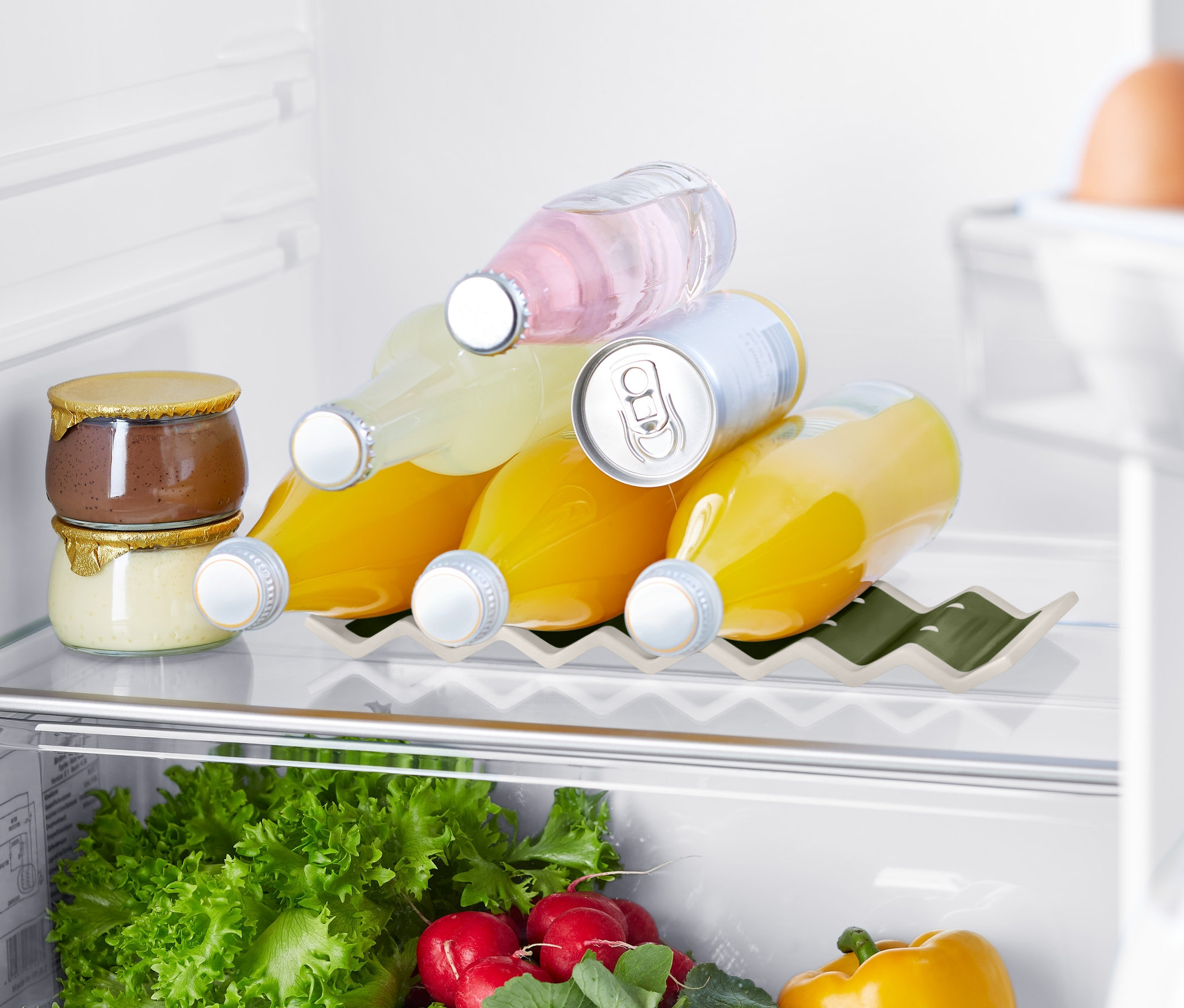 Dans le réfrigérateur, il y a des confitures, des boissons dans un support de bouteilles pour réfrigérateur, des légumes et des œufs.