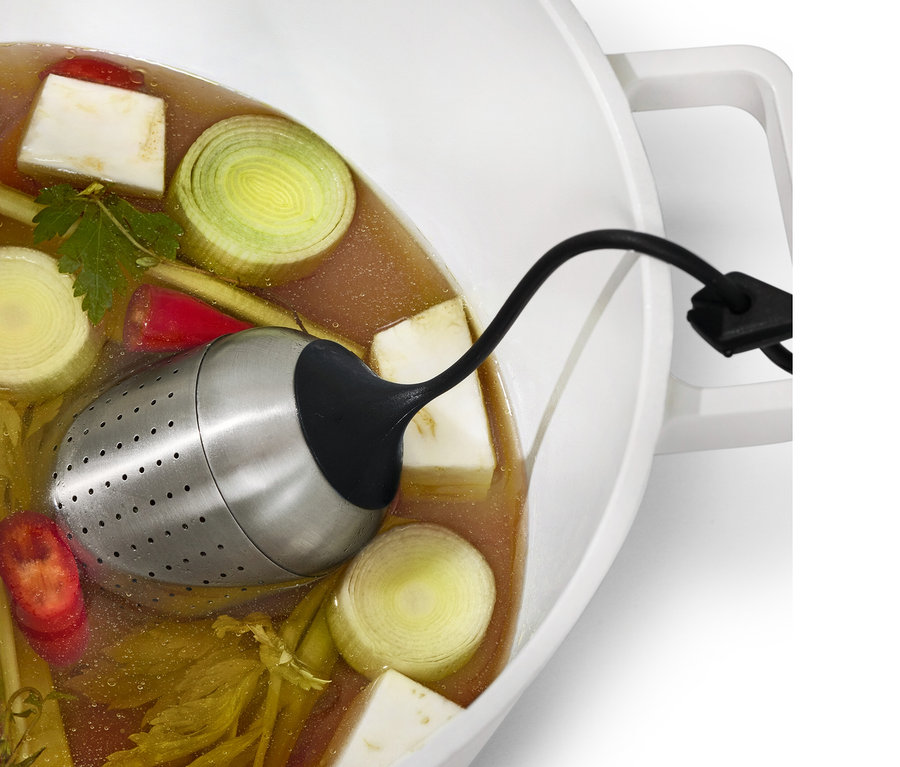 Une boule à épices est suspendue dans une casserole avec du bouillon et des légumes.