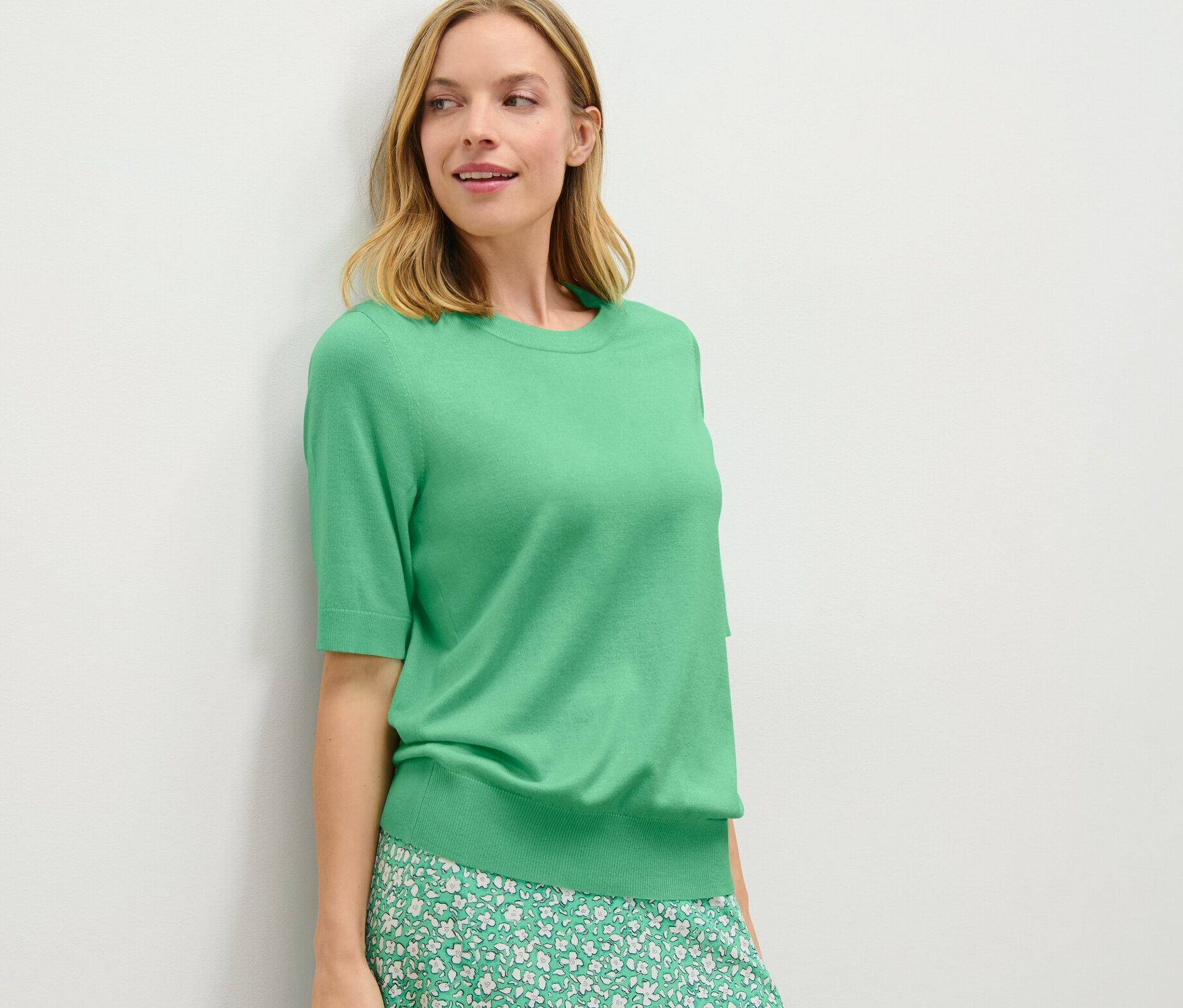 Femme posant en pull en maille fine vert et jupe à fleurs.