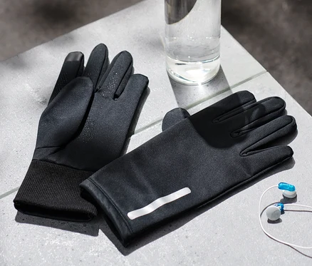 Deux gants thermiques noirs pour la protection contre le vent, une bouteille d'eau et des écouteurs sont posés sur une surface grise.