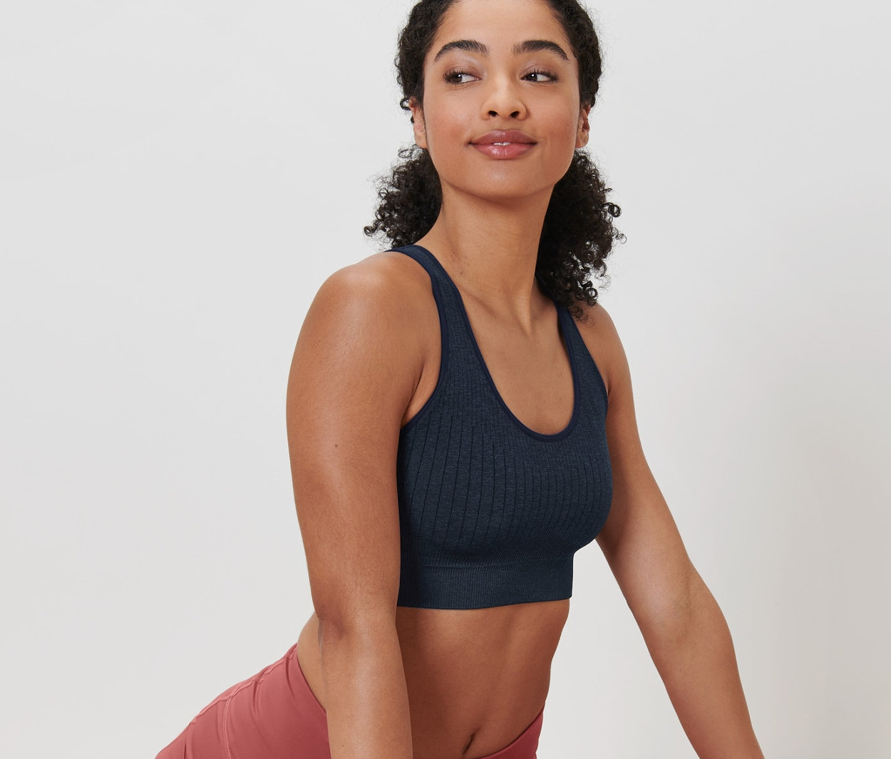 Femme portant une brassière de sport sans coutures bleu foncé et un legging rose faisant des étirements sur un tapis.