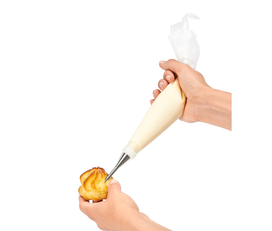 Une main remplit de crème un chou à la crème à l'aide d'un lot de poches à douilles.