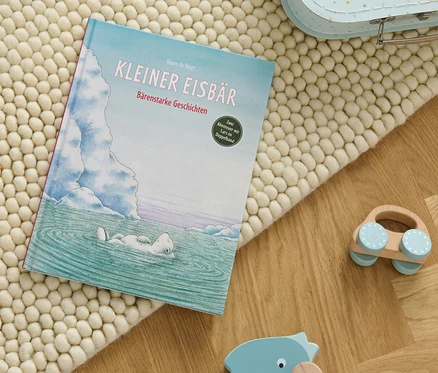 Le livre « Kleiner Eisbär – bärenstarke Geschichten » posé sur un tapis beige à côté de jouets en bois.