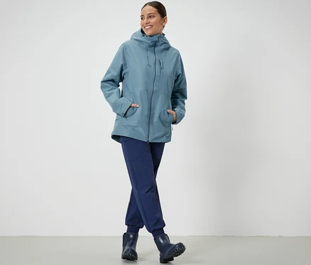 Une femme debout pose dans une veste technique outdoor bleu clair.