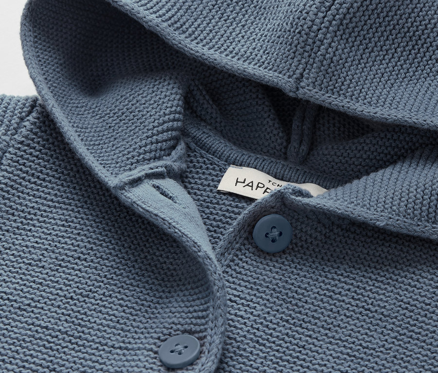 Gros plan sur un cardigan bleu en tricot avec capuche et boutons.