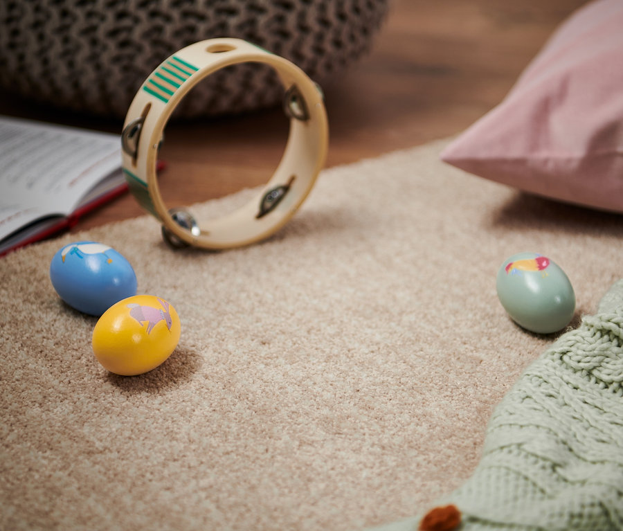 Sur un tapis beige reposent un livre ouvert, un tambourin et trois maracas.