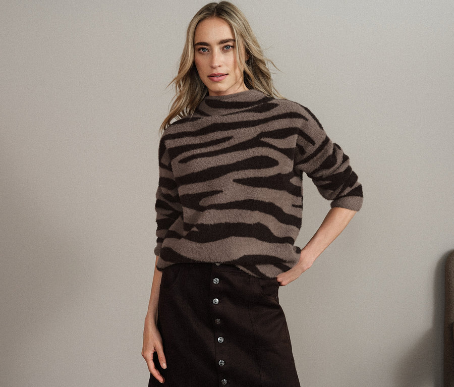 Femme posant en pull marron et noir à motif animalier et jupe marron.
