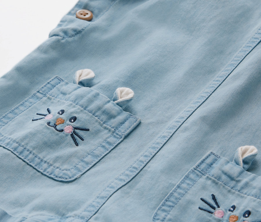Détail d'une salopette en chambray pour enfant avec une broderie de lapin sur la poche.