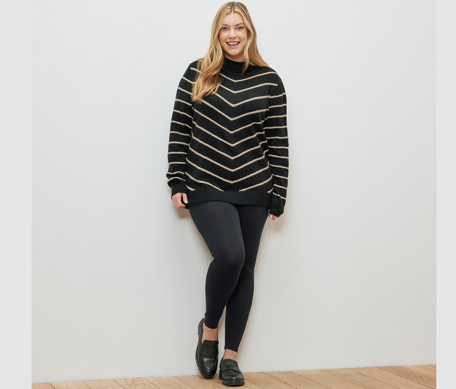 Une femme pose, portant un pull noir rayé en maille à col montant et un legging.
