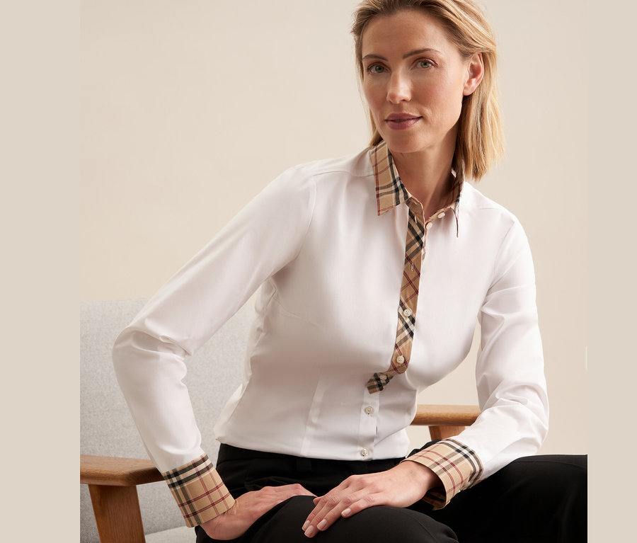 Une femme assise sur une chaise porte une chemise en popeline à carreaux Seidensticker blanche.