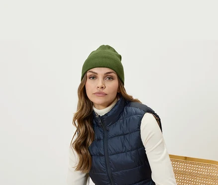 Portrait d'une femme aux cheveux bruns portant un bonnet olive et un gilet matelassé bleu marine.