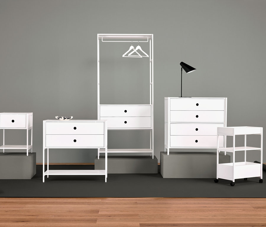 Agencement de meubles blancs avec table de chevet, commode à tiroirs, portant à vêtements, lampe et étagères.