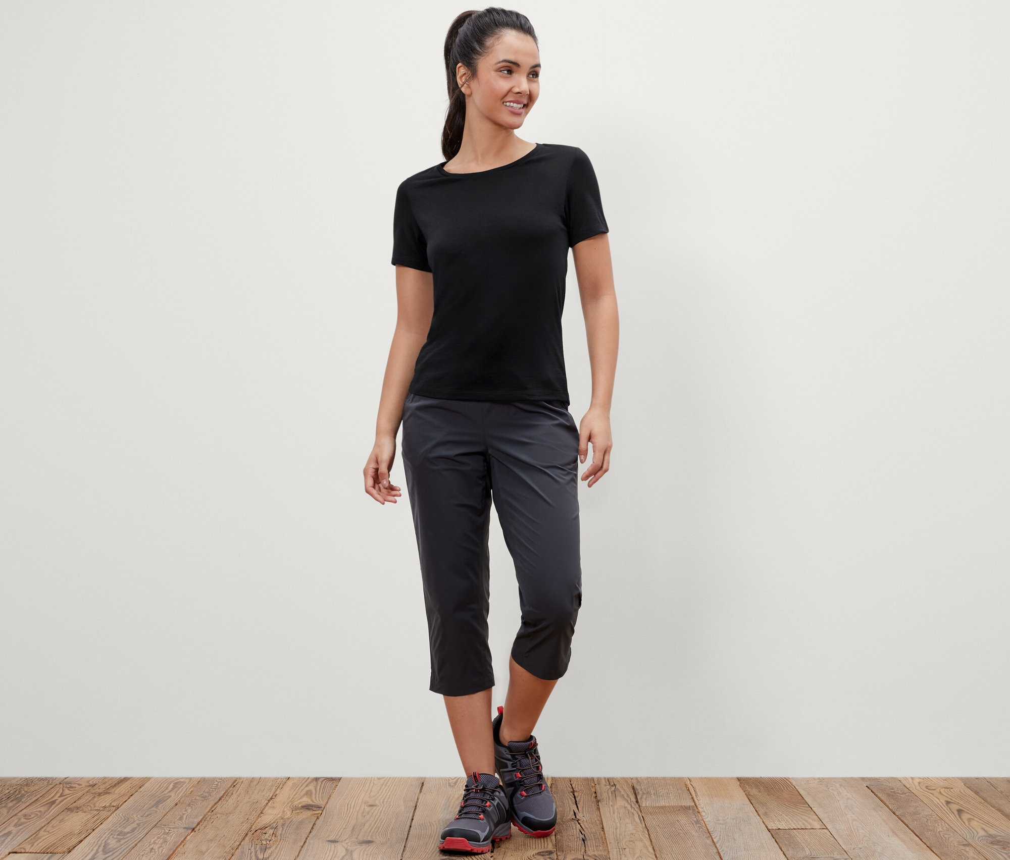 Femme posant en t-shirt noir avec laine mérinos et pantalon capri gris foncé.