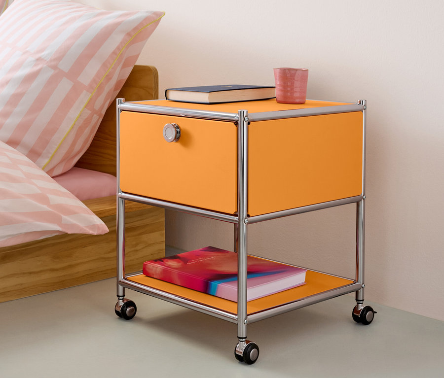 Table d’appoint orange avec tiroir en métal « CN3 » à côté d’un lit.