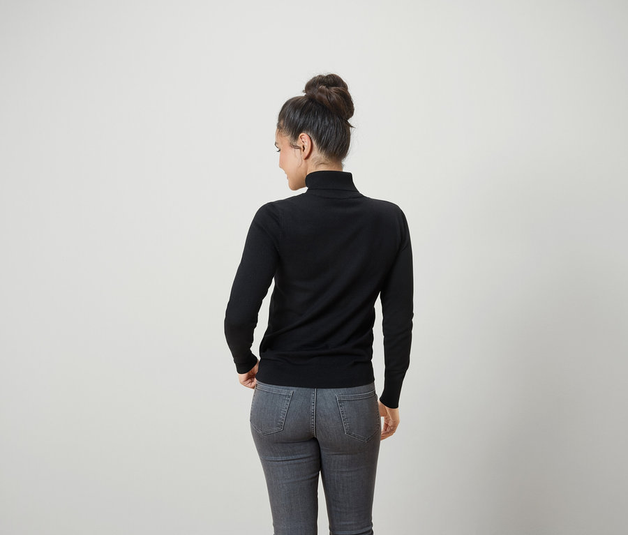 Vue de dos d'une femme aux cheveux attachés en chignon portant un pull à col roulé noir et un jean gris.